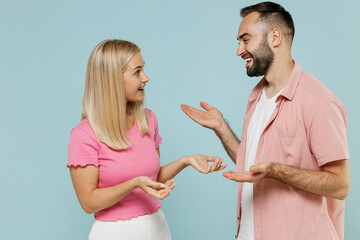 Young fun couple two friends family man woman in casual clothes looking to each other talk speak together isolated on pastel plain light blue color background studio portrait People lifestyle concept.