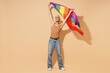 Full body young activist bisexual happy fun blond latin gay man with make up in beige tank shirt waving hold rainbow flag isolated on plain light ocher background studio People lgbt lifestyle concept