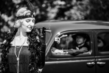 Young woman standing near retro car where man sits