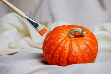 Artistic brush with orange paint and a beautiful ripe pumpkin lie on sacking. Preparing for Halloween. Autumn products for a healthy diet.