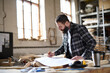 © Halfpoint - Low angle view of mature male carpenter looking at blueprints plans in carpentery workshop. Small business concept.