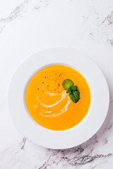 Wall Mural - Flat lay of pumpkin soup on white background with cream and mint garnish