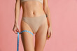 © master1305 - Close-up slim female body with well kept skin in pastel color panties using centimeter isolated over pink studio background.