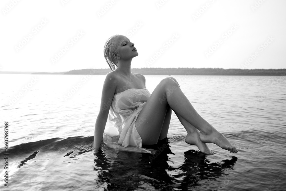 Art nude sexy blonde with short haircut is sitting in water on shore