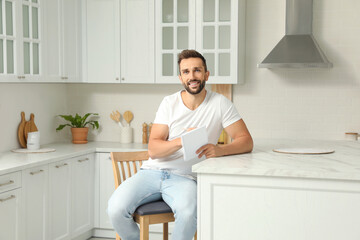 Wall Mural - Handsome man with notebook sitting on stool in kitchen