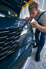 Car service worker installs headlight protection film with squeegee