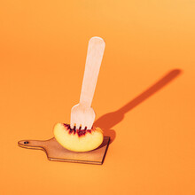 Slice Of Fresh Peach On A Wooden Fork Served On A Chopping Board.  Minimal Fruit Concept On Orange Background.