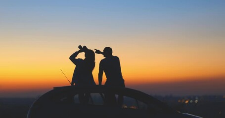 Wall Mural - Couple stargazing together with binoculars from a car's roof on a countryside suburban area.