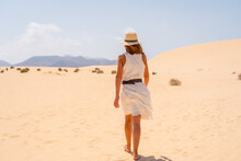 A Young Tourist Wearing A Hat Walking Along The Sand On The Beaches Of The Corralejo Natural Park, Fuerteventura, Canary Islands. Spain