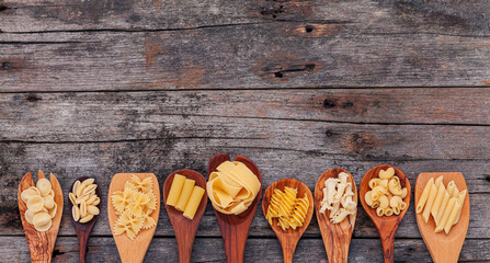 Wall Mural - Italian foods concept and menu design . Various kind of pasta elbow macaroni ,farfalle ,rigatoni ,gnocco sardo in wooden spoons setup on wooden background.