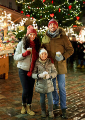 Poster - family, winter holidays and celebration concept - happy mother, father and little daughter with takeaway drinks at christmas market on town hall square in tallinn, estonia over lights