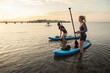 © Maskot - Female friends standing by paddleboard in sea