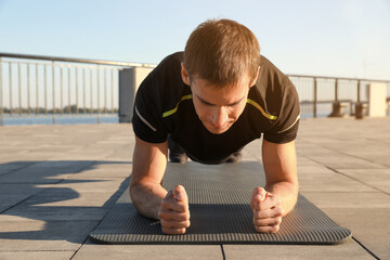 Canvas Print - Sporty man doing plank exercise on mat outdoors