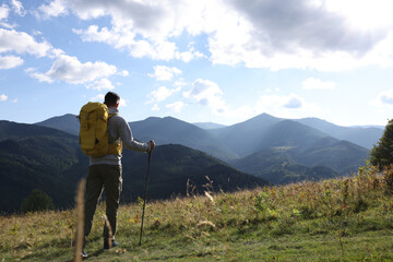 Wall Mural - Tourist with backpack and trekking poles enjoying mountain landscape, back view. Space for text