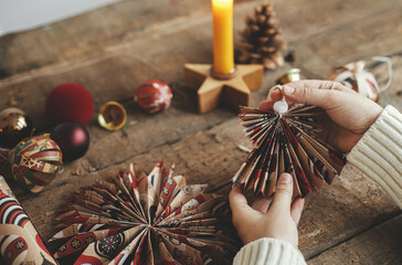 stylish handmade angel from festive red wrapping paper in hands on background of rustic wooden table