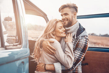 Poster - Beautiful young loving couple embracing while standing near minivan outdoors