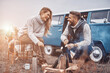 © gstockstudio - Beautiful young loving couple having picnic by the bonfire while sitting near their retro minivan