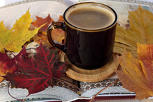 A Cup Of Coffee On A Wooden Stand Surrounded By Autumn Maple Leaves On A Centerfold Book In Sunlight