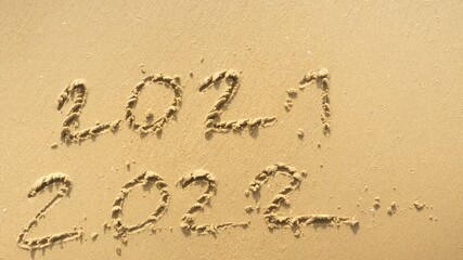 Wall Mural - message year 2021 replaced by 2022 written on beach sand background. good bye 2021 hello to 2022 lap