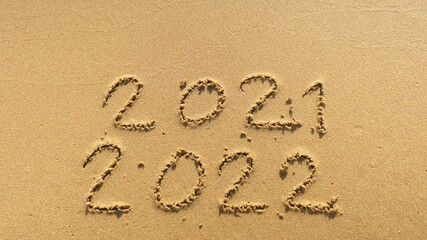 Wall Mural - message year 2021 replaced by 2022 written on beach sand background. good bye 2021 hello to 2022 lap