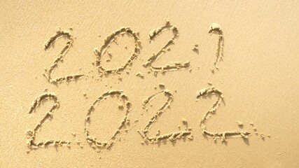 Wall Mural - message year 2021 replaced by 2022 written on beach sand background. good bye 2021 hello to 2022 lap