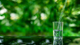 Fototapeta Łazienka - Water flows into a glass placed on a wooden bar.