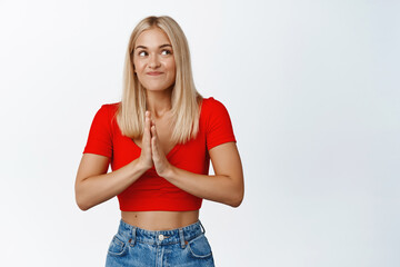 Wall Mural - Hopeful smiling girl waiting with excitement, rub hands and waits for relish, waiting for good news, standing in summer outfit against white background