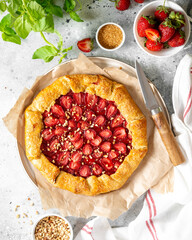 Wall Mural - French galette or pie with strawberries and almonds on baking paper on a light gray culinary background top view. Summer homemade sweet pastries	