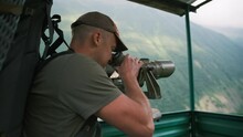 A tourist looks through binoculars at the border outpost. A man conducts remote observation through the lens of binoculars on an observation tower.