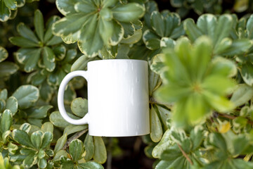 White porcelain mug cup isolated on green plants background with copy space. Mock up for design. 