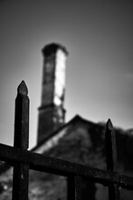 Black Metal Fence Against Of A Building With A High Chimney. Black And White. Holocaust Theme. Concept