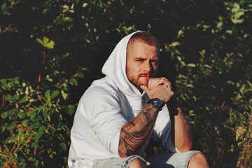 Wall Mural - Portrait of young bearded man with tattoos in white jacket in countryside