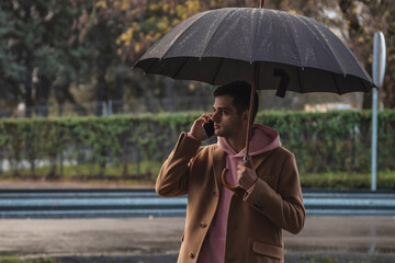 man on the street with umbrella and mobile phone
