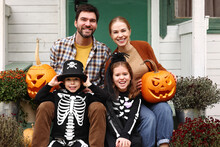 Young Happy Family Parents With Kids Standing On House Porch During Halloween Holidays