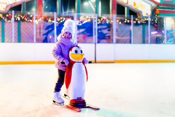 A little girl is skating on an ice rink, holding on to a support, a child is learning to skate, winter entertainment for children