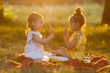 Two Little Mixed Race Girls Play, Talk And Share Secrets In The Park Outdoors Sitting On A Blanket On A Warm Sunny Summer Day. Walking In The Fresh Air, Concept Of A Healthy Lifestyle. 