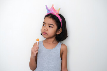 Wall Mural - Asian little kid glancing to her side with annoyed face expression while holding lolipop candy