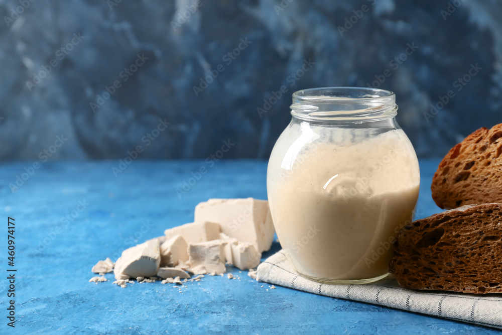 Glass jar with fresh sourdough and bread on blue background