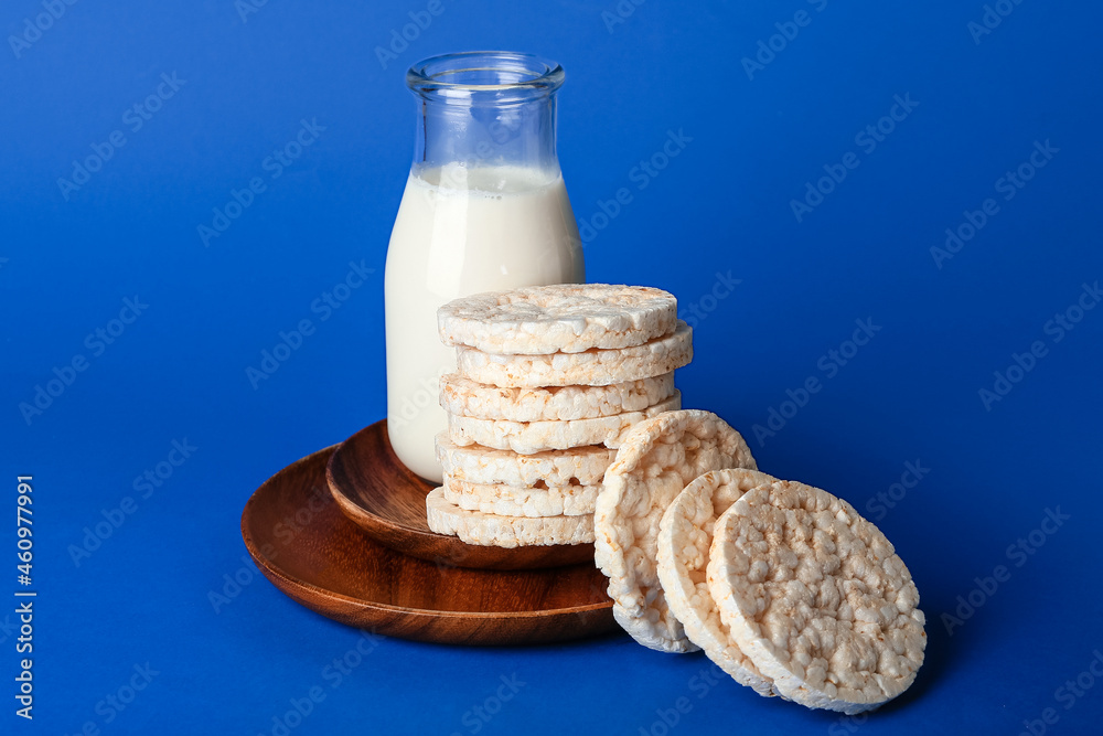 Puffed rice crackers and bottle of milk on color background