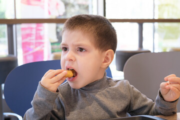 A boy of 4 years old eats nuggets with sauce in a fast food cafe.