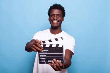 Portrait of man holding clapperboard to cut scenes in movie making industry. Casual person showing board to camera and smiling while having filmmaker object for cinematography