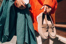 Close-up Photo Of Fashionable Women In Orange Sweater And Beige Dress Holding In Hands Checkered Coat And Beige Suede Shoes