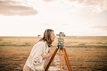 Mature Woman Looking Through Theodolite At Field