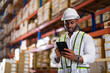 © structuresxx - Warehouse worker working process checking the package with a tablet in a large distribution center. an African male supervisor inspects cargo delivery status.