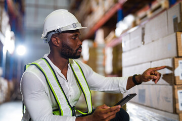 Wall Mural - Warehouse worker working process checking the package with a tablet in a large distribution center. an African male supervisor inspects cargo delivery status.