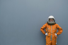 Astronaut Wearing Orange Space Suit And Space Helmet Smiling While Posing Against Gray Wall Background