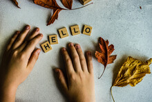 Hands Spelling Out The Word Hello Using Wooden Blocks And Autumn Leaves On A Table