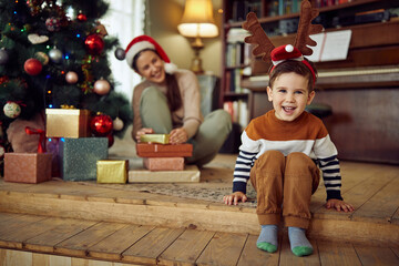 Wall Mural - Cheerful boy wears reindeer antlers and has fun on Christmas day at home.