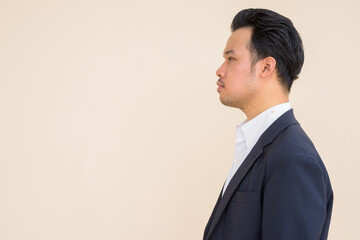 Wall Mural - Profile view of Asian businessman wearing suit against plain background