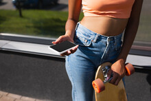 cropped view of african american woman holding longboard and smartphone with blank screen